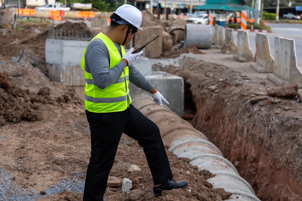 Civil engineer supervising the installation of concrete drainage pipes at a roadside construction site