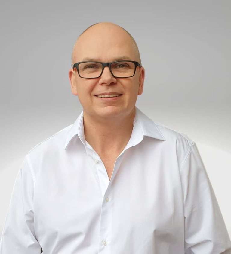 Headshot of a middle-aged man wearing glasses and a white shirt, smiling at the camera against a gray background